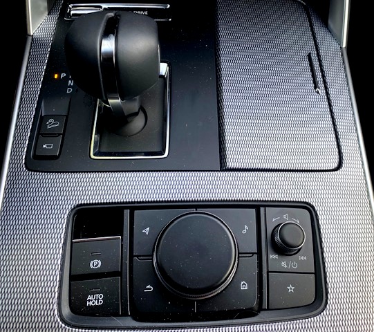 Very wide centre console houses Mazda's infotainment control and volume-on-off knob. Notice the shift pattern in the upper left part of the photo that shows the Park position to the left of the gear positions. The painted pattern on the alloy look trim appears busy to some observers